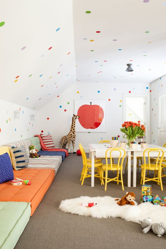 a fun and bold kids' playroom with sofas lining up the wall, a creativity zone, polka dot walls and a ceiling and bright toys