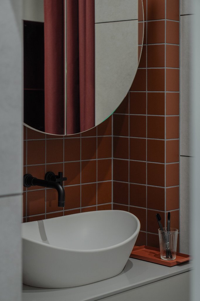 The bathroom is done with rust-colored tiles, a round mirror and a vessel sink