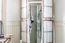 16 a vintage bathroom with a modern shower space but clad with old window frames and with white fabric hanging