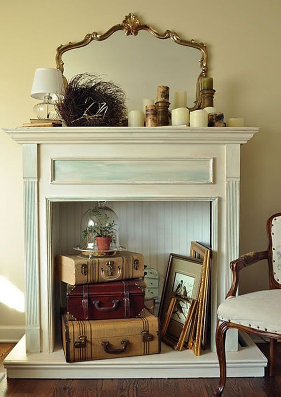 a vintage fireplace with vintage suitcases, picture frames, a cloche with greenery and candles on the mantel