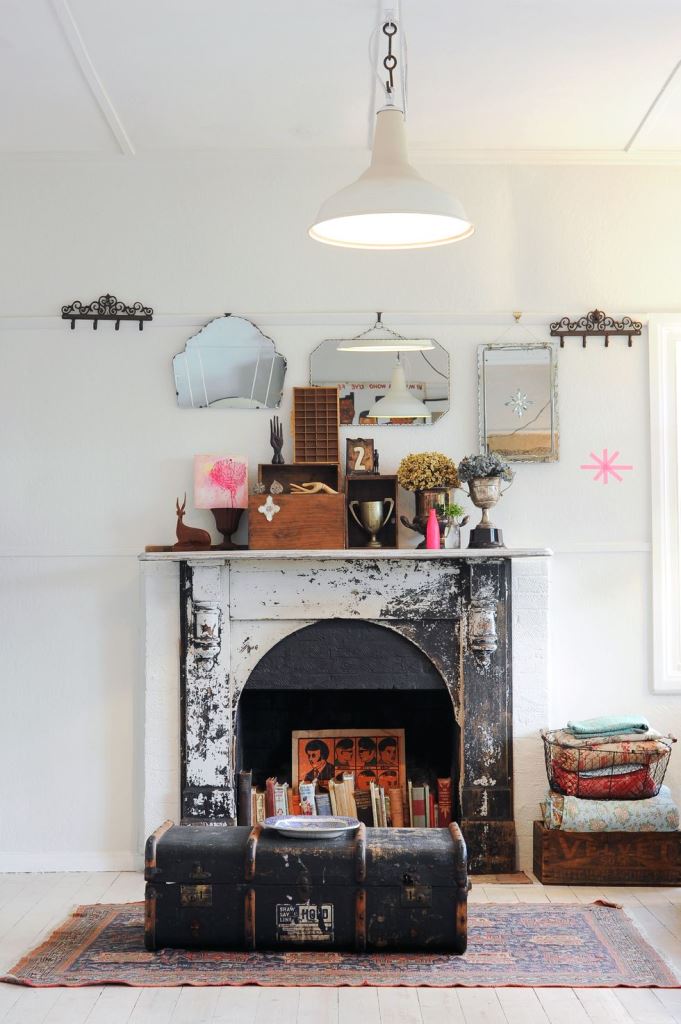 a shabby cihc fireplace with books and a bold artwork looks statement-like and bold, a suitcase in front of it adds vintage charm