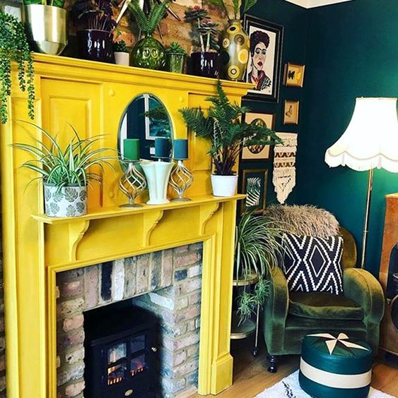 a brick fireplace with a sunny yellow surround, lots of plants and candles is a very cozy idea and a fresh take on a traditional fireplace