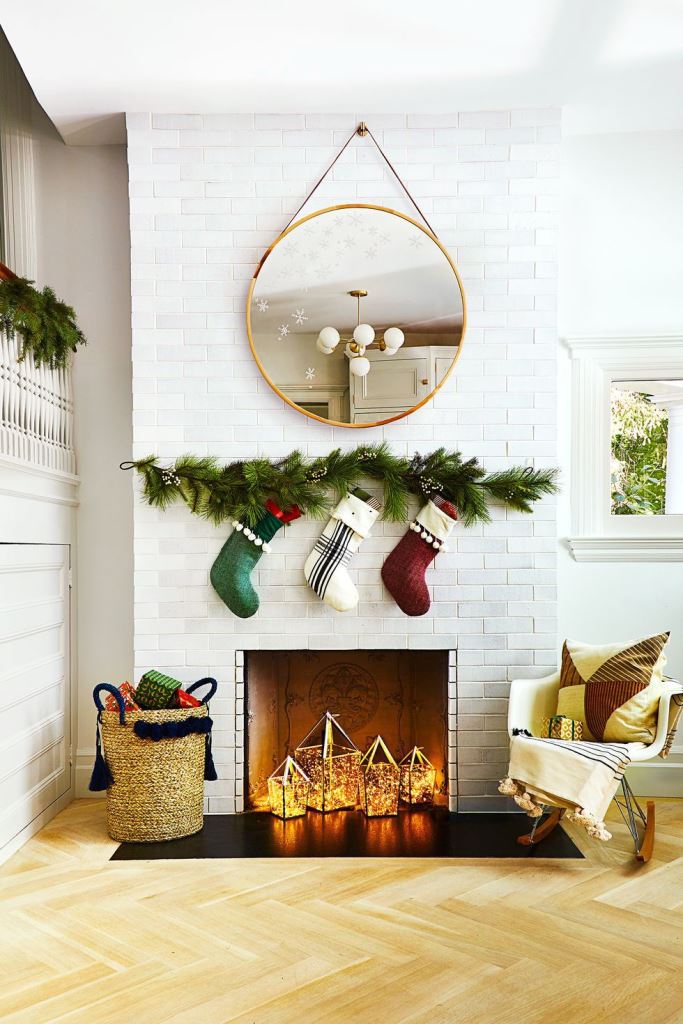 a non-working fireplace styled for Christmas with some stockings hanging over it and with lights lanterns inside it