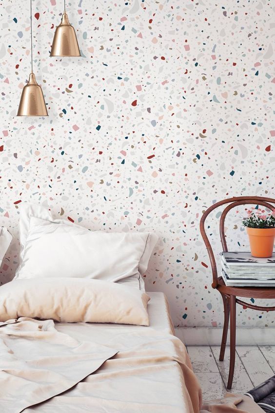 a pretty modern bedroom with a terrazzo pattern accent wall, brass lamps and a dark stained chair