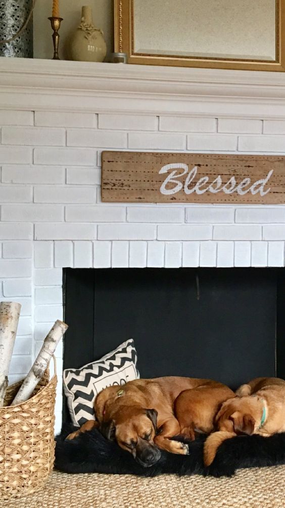 a non-working fireplace with white brick and a furry bed for two dogs inside it, with pillows