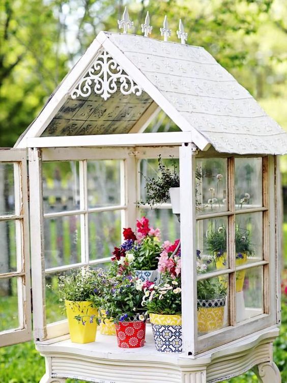 a small greenhouse made of old window frames, with bright planters and greenery and flowers is a cool DIY