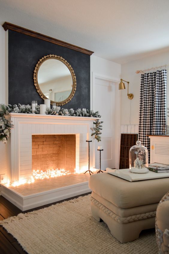 a winter non-working fireplace with lights inside it, snowy fir garland, candles and a mirror over the mantel