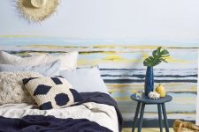 a beachy bedroom in bold colors – blue, navy, yellow, with a large comfy bed, a striped accent wall, knit and crochet bedding and rugs