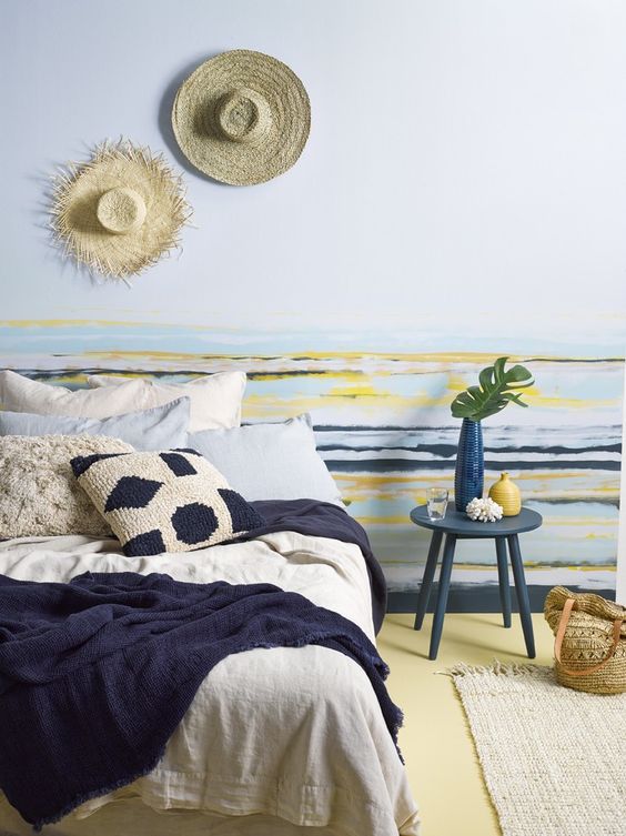 a beachy bedroom in bold colors - blue, navy, yellow, with a large comfy bed, a striped accent wall, knit and crochet bedding and rugs