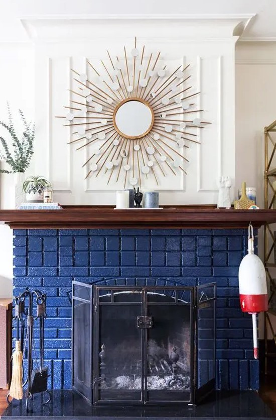 a beautiful and chic navy brick fireplace with a metal screen, a stained mantel with decor, a sunburst mirror over the mantel