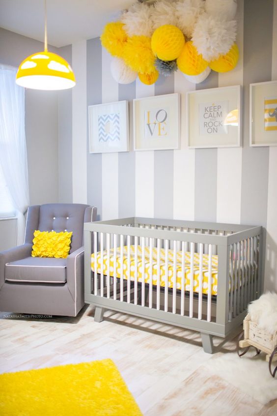 a bold grey, white and yellow nursery with a vertical stripe wall, a paper pompom arrangement, a grey chair and a yellow lamp
