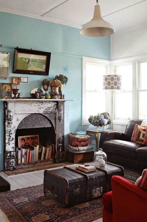 a bright living room with blue walls, a fireplace with a shabby chic mantel, with books, with a chest coffee table and a brown sofa is chic