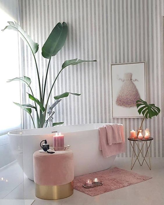 a charming girlish bathroom with a striped grey and white wall, a pink ottoman, a refined table and pink textiles