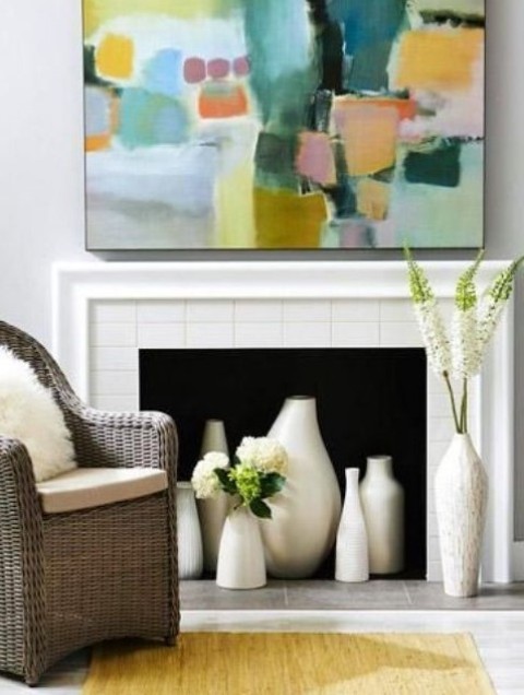 a chic and bright nook with a fireplace clad with tiles, lots of beautiful vases, a wicker chair and a colorful artwork
