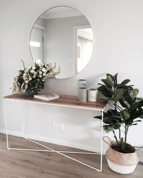 a chic modern entry with a wooden console, a round mirror and some potted plants and vases