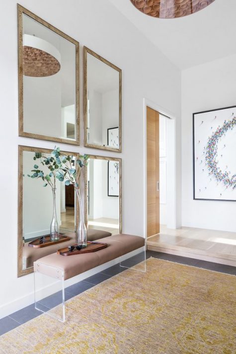 a chic modern entryway with a gallery wall of mirrors, a leather and acrylic bench and greenery in a vase