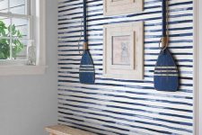 a coastal entryway with blue watercolor stripes, artworks and oars, a wooden bench and a basket is very bold
