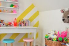 a colorful kids’ playroom accented with a yellow and white striped wall and lots of bold toys