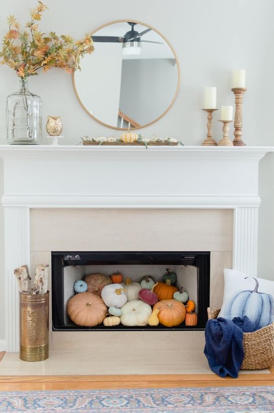 a contemporary fireplace with colorful pumpkins inside, firewood and a blue pumpkin pillow plus some leaves on the mantel