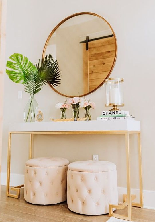 a fabulous modern entryway with a white console, blush storage ottomans, a round mirror and a candle