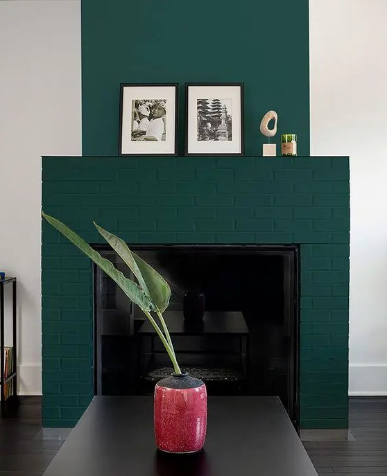 a forest green brick fireplace with some decor on the mantel, a black coffee table and a cool coral vase with leaves