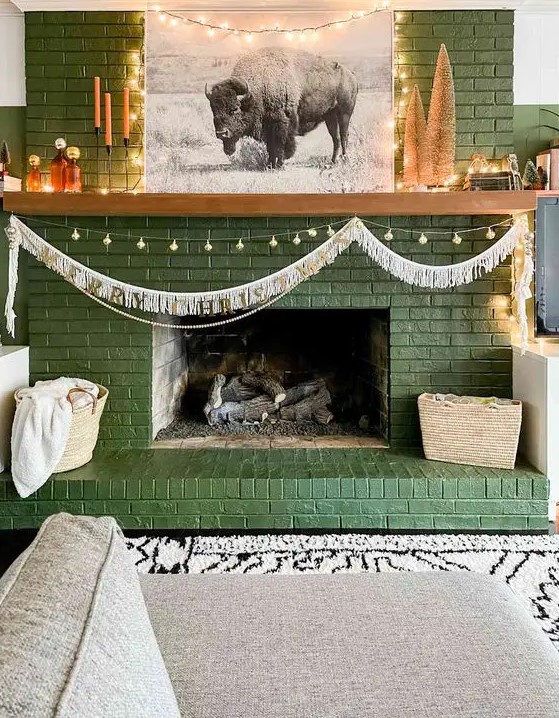 a green brick fireplace with lights and a garland, with decor, candles and artwork is a cool and lovely decoration