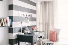 a light-filled home office with a black and white striped accent wall, a black desk, a white chair, neutral textiles and pink touches is very chic