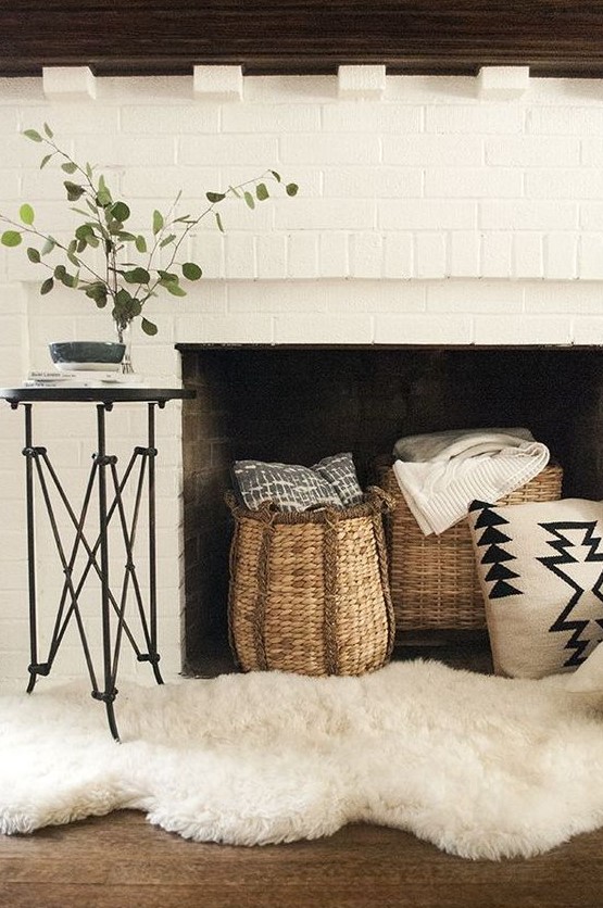 a lovely white brick fireplace with a dark stained mantel with baskets for storing blankets and pillows and a faux fur rug
