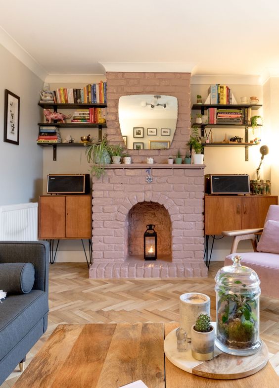 a mid-century modern living room with cabinets, open shelves, a mauve brick fireplac,e a grey sofa, a pink chair and a coffee table