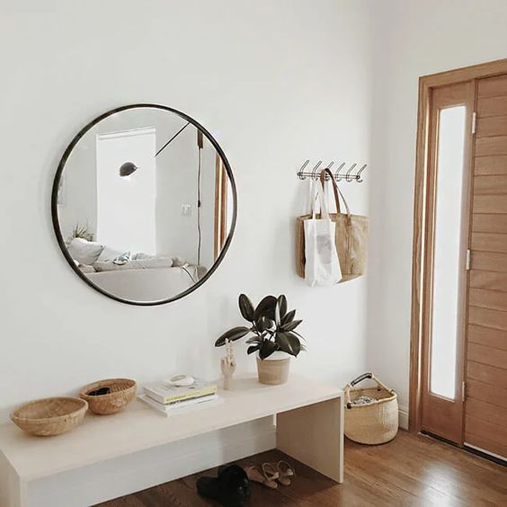 a modern entry with a sleek bench, a round mirror, some baskets and a clothes rack is stylish and looks ethereal