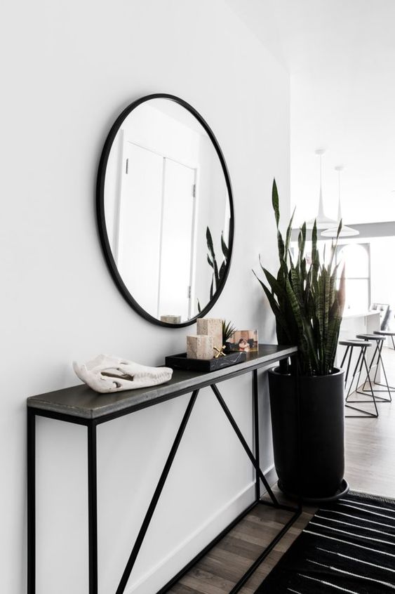 a modern entryway with a black narrow console, a round mirror, a statement plant and some decor