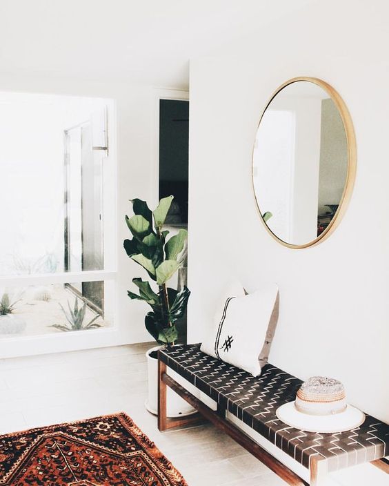 a modern entryway with a leather woven bench, a boho rug and a round mirror plus a statement plant