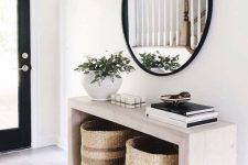 a modern entryway with a sleek wooden console, baskets for storage, a round mirror and a potted plant