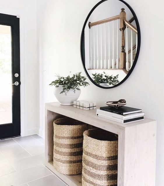 a modern entryway with a sleek wooden console, baskets for storage, a round mirror and a potted plant