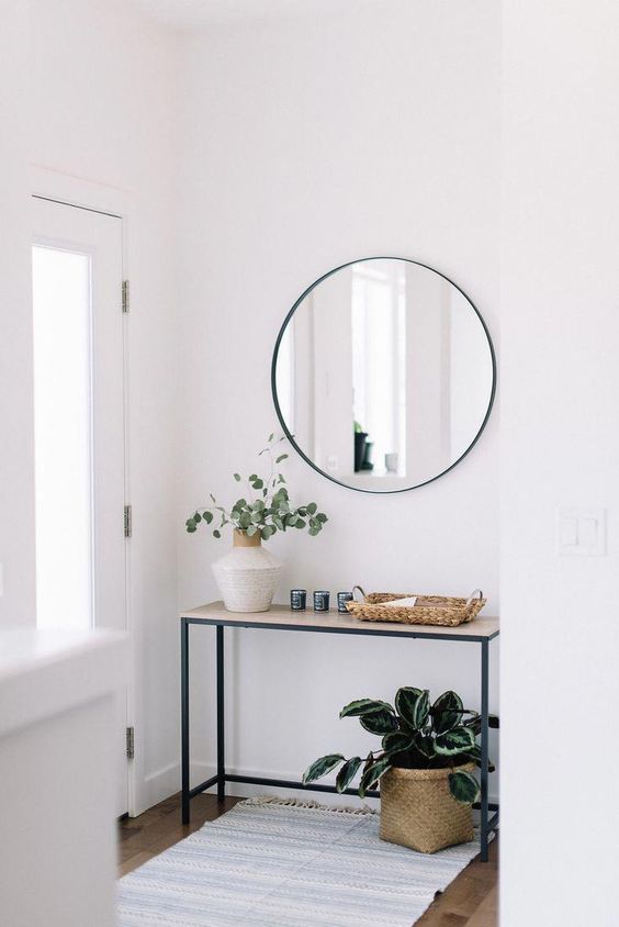 a modern front entry with a narrow console, a round mirror, potted plants and baskets is very welcoming