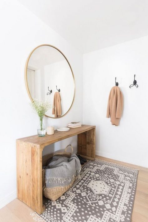 a modern warm-colored entry with a wooden bench, a round mirror, a printed rug and a basket with a blanket