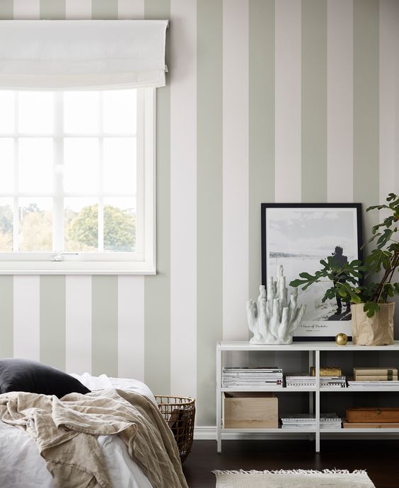 a neutral and ethereal bedroom with a green and white striped wall, neutral textiles and potted plants is very beautiful