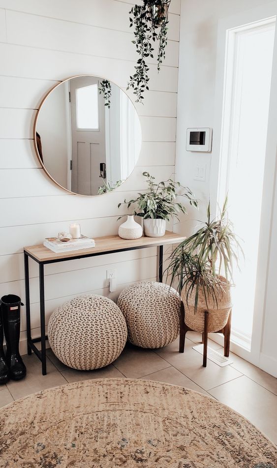 a neutral modern entryway with a wooden console, crochet ottomans, potted plants and a round mirror is chic