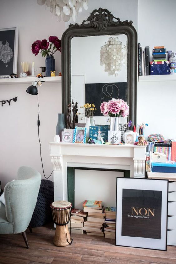 a non-working fireplace with books, an artwork, photos and blooms on the mantel and some decor