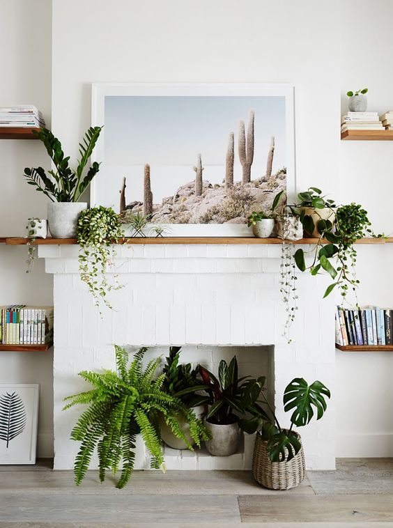 a non-working white brick fireplace with potted plants, potted greenery on the mantel and an artwork