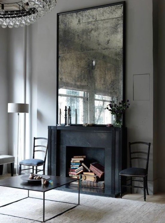 a refined living room with a black fireplace that is used for book storage and a vintage mirror for a more exquisite look in the space