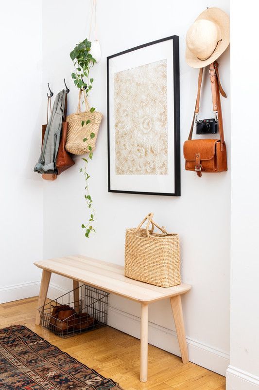 a simple modern entry with a wooden bench, a statement artwork, a wire basket and clothes hangers
