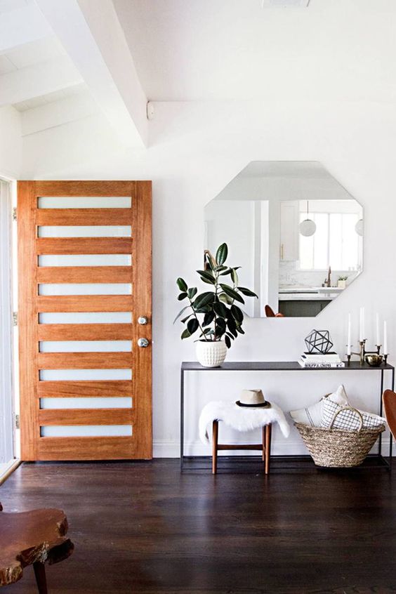 a simple modern entryway with a geometric mirror, a black console, stools and a basket with pillows