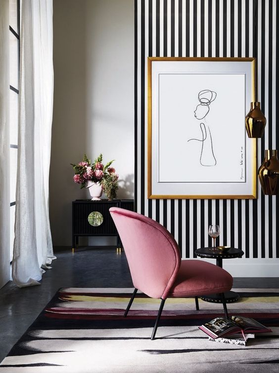 a sophisticated living room with a black and white accent wall, a pink chair and a pretty artwork and refined furniture