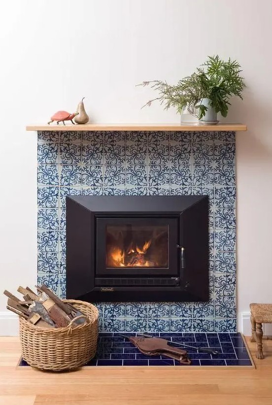 a stylish fireplace clad with blue patterned tiles around and blue glossy ones on the floor plus a simple wooden mantel is very vibrant