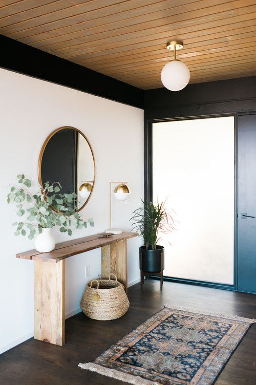 a stylish modern entryway with a round mirror, a basket, a plant on a stand and a boho rug