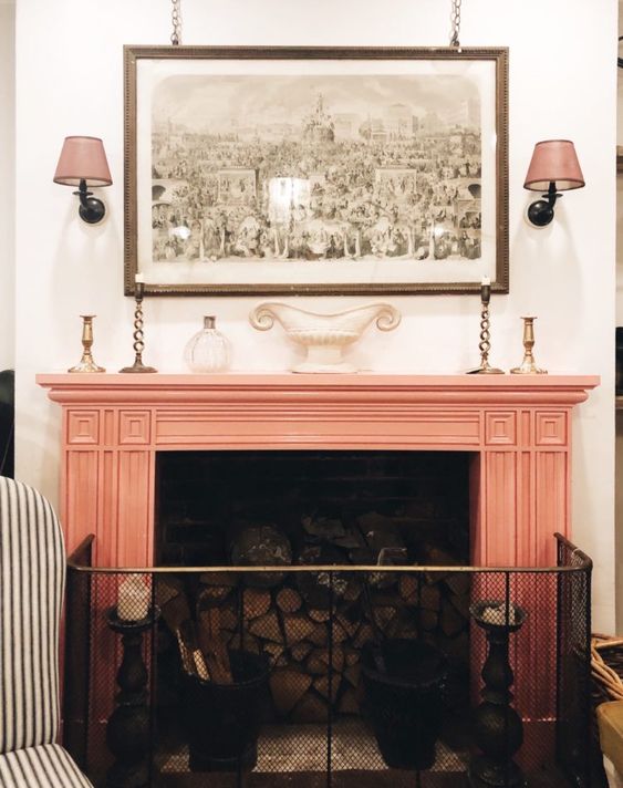 a vintage fireplace with a slamon pink mantel and a wire screen, an artwork and wall sconces is a pretty addition to your living room