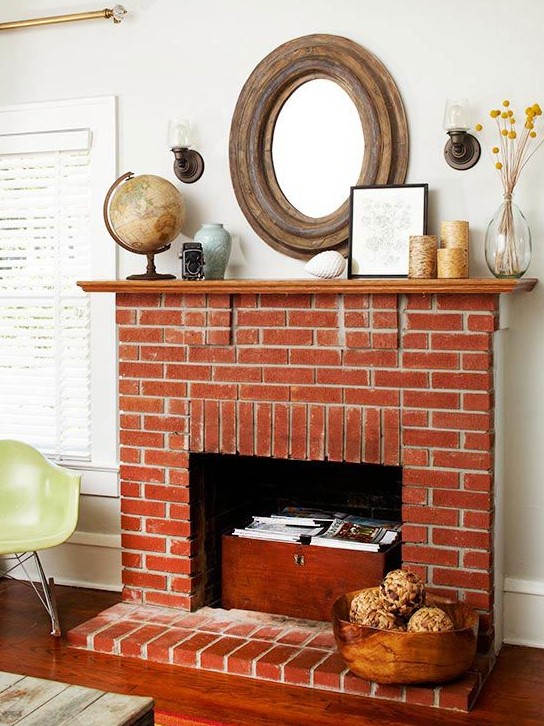 a vintage red brick fireplace with a wooden chest that is used for books and magazine storage, with pretty vintage decor on the mantel