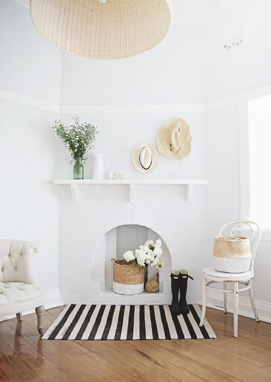an airy space with chic chairs, a brick fireplace with a basket and white blooms, hats and vases is very cozy and welcoming