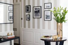 an art decor entryway with a grey and white striped wall, white paneling, a stylish gallery wall and dark furniture